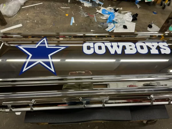 Dallas Cowboys-themed casket with a glossy silver finish, silver panels, and the team's star logo, displayed closed in a showroom setting