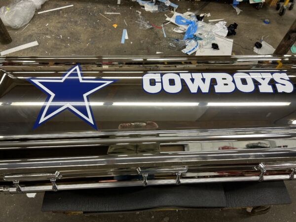 Chrome casket with a blue star and "COWBOYS" written on the lid. Workshop setting with scattered tools and materials in the background.