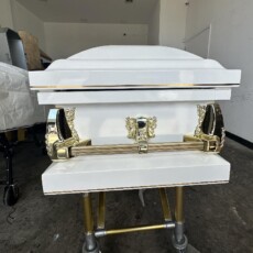 White casket with gold handles on a wheeled trolley in a plain room. The polished surfaces reflect light, creating a somber, respectful atmosphere.