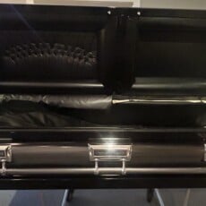 Open black casket with a padded interior is seen in a showroom. Its sleek design and polished metal handles reflect a somber, respectful tone.