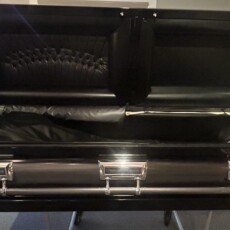 Open black casket with a padded interior is seen in a showroom. Its sleek design and polished metal handles reflect a somber, respectful tone.
