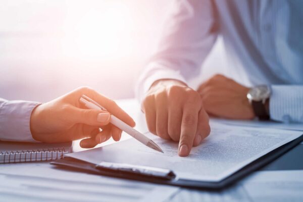 Close-up of two people pointing and writing on documents at a desk, with pens, paper, and soft natural light.