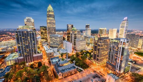 Aerial view of a vibrant city skyline at dusk with illuminated skyscrapers and streets. The scene conveys a bustling, lively urban atmosphere.