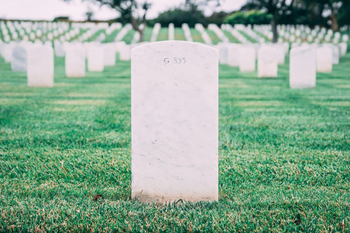 Rows of white headstones in a military cemetery stretch into the distance, set on lush green grass, evoking a solemn and respectful atmosphere.