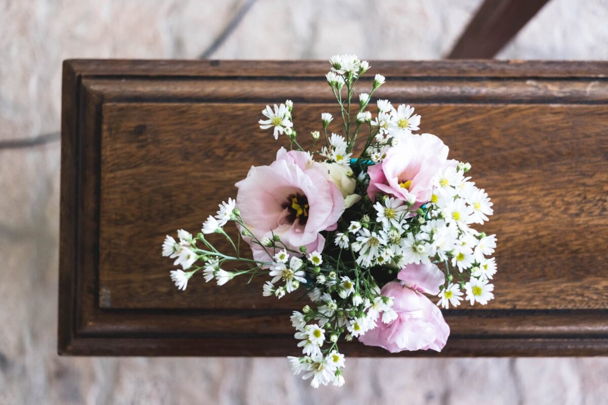 Top view of a wooden casket with a small floral arrangement of pink lisianthus and white baby’s breath flowers.