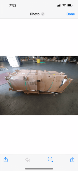 A large, crumpled cardboard box sits on a warehouse floor. It appears damaged, with several dents and tears, reflecting a chaotic, worn-out state.