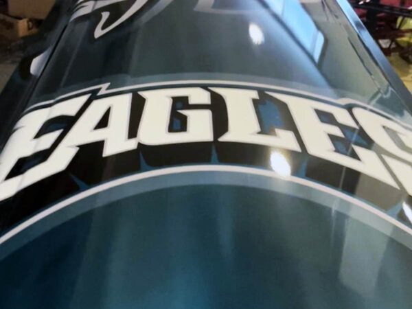 Close-up of the word "Eagles" in bold white letters on a shiny, metallic green surface, possibly a vehicle, conveying a sporty and dynamic tone.