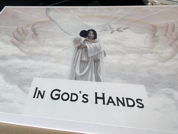A serene image shows a woman in white hugging an infant, surrounded by clouds, large protective hands, wings, and a dove. Text reads "In God's Hands."