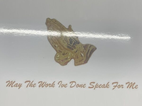 Alt text: Gold praying hands against a white background, with the text "May the work I've done speak for me" in elegant brown script below, conveying reflection and humility.